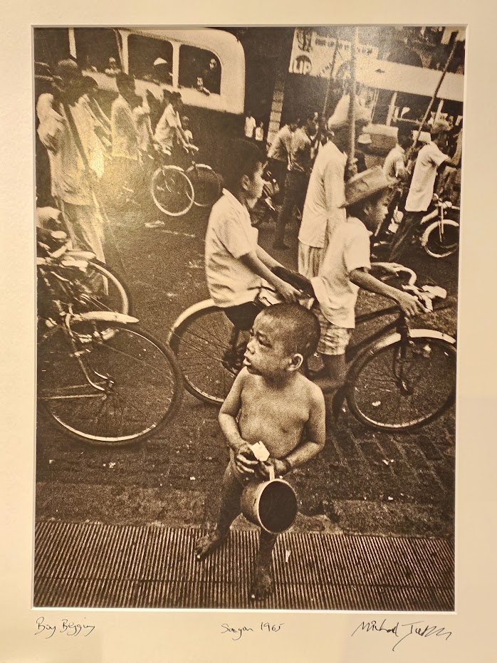 South Vietnam, boy begging in street while world carries on around him by Michael Joseph