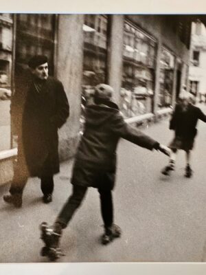 Pair of kids skating in parisian street with an onlooker in a beret by Michael Joseph