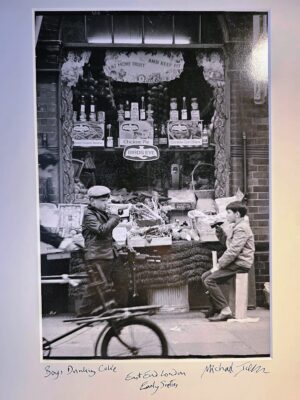 Boys drinking coke, under "eat more fruit and keep fit" sign, sixties photo taken in East End London by Michael Joseph