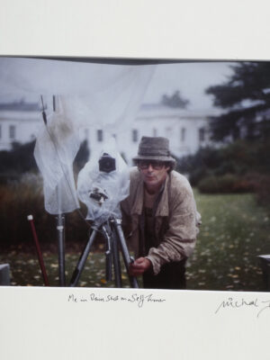 The photographer on a photo-shoot in the rain with a self-timer, castle-type building behind by Michael Joseph