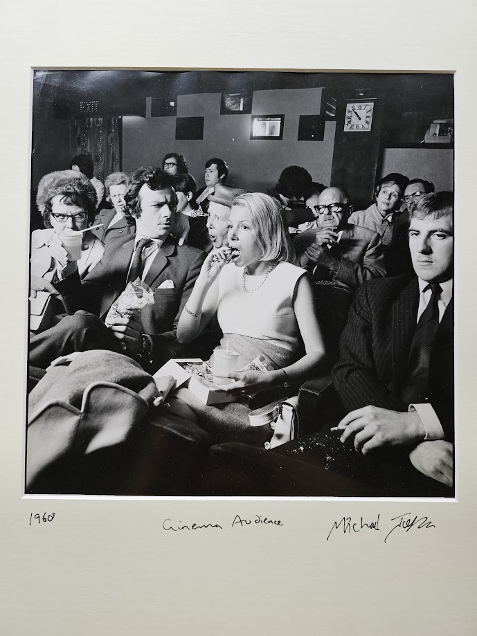 Femme des années 60 en train de manger au cinéma, avec son voisin visiblement agacé – les émotions à leur comble